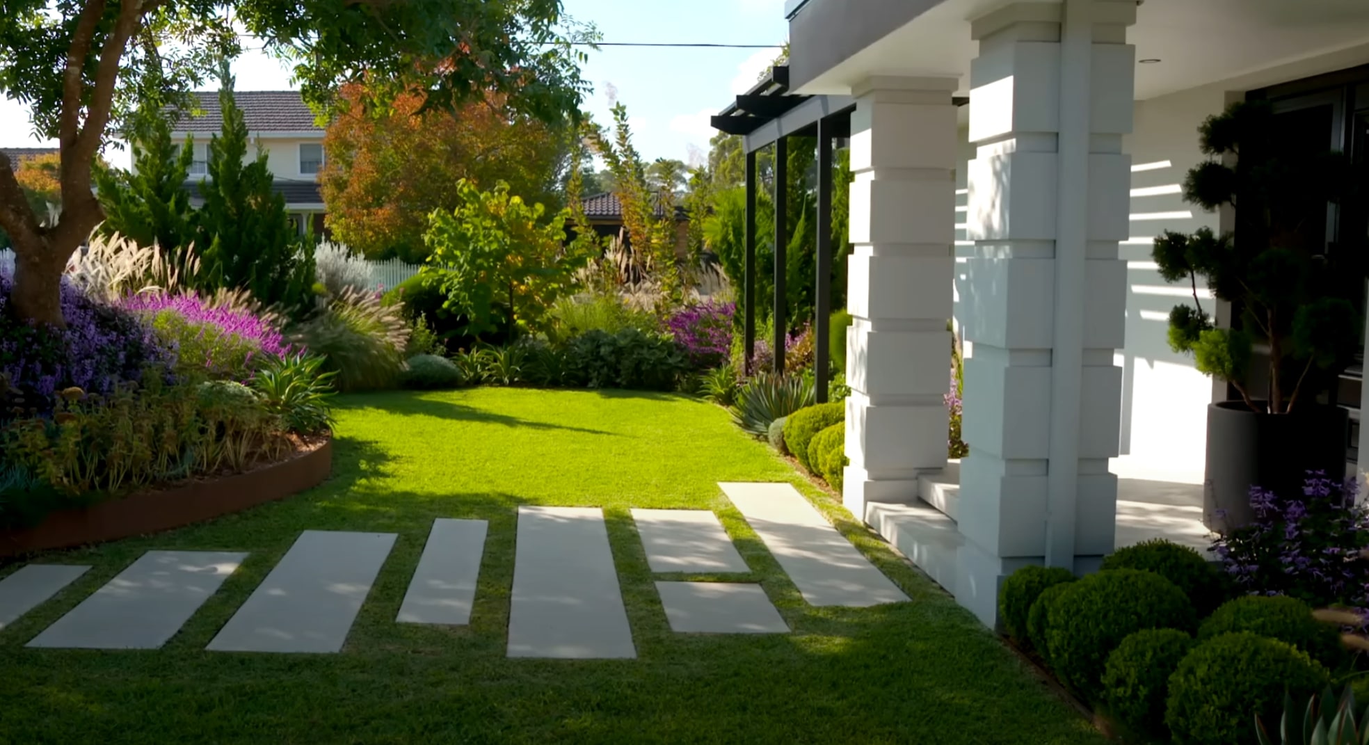 Elegant modern garden with concrete pavers, lush lawn, and colorful flowering plants