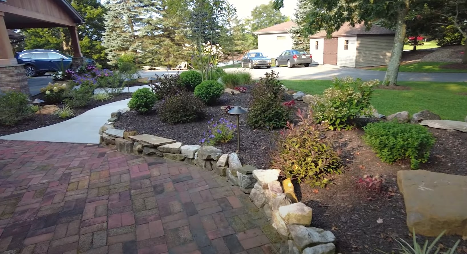 Front yard landscape renovation featuring natural stone retaining walls, colorful plantings, and brick paver driveway