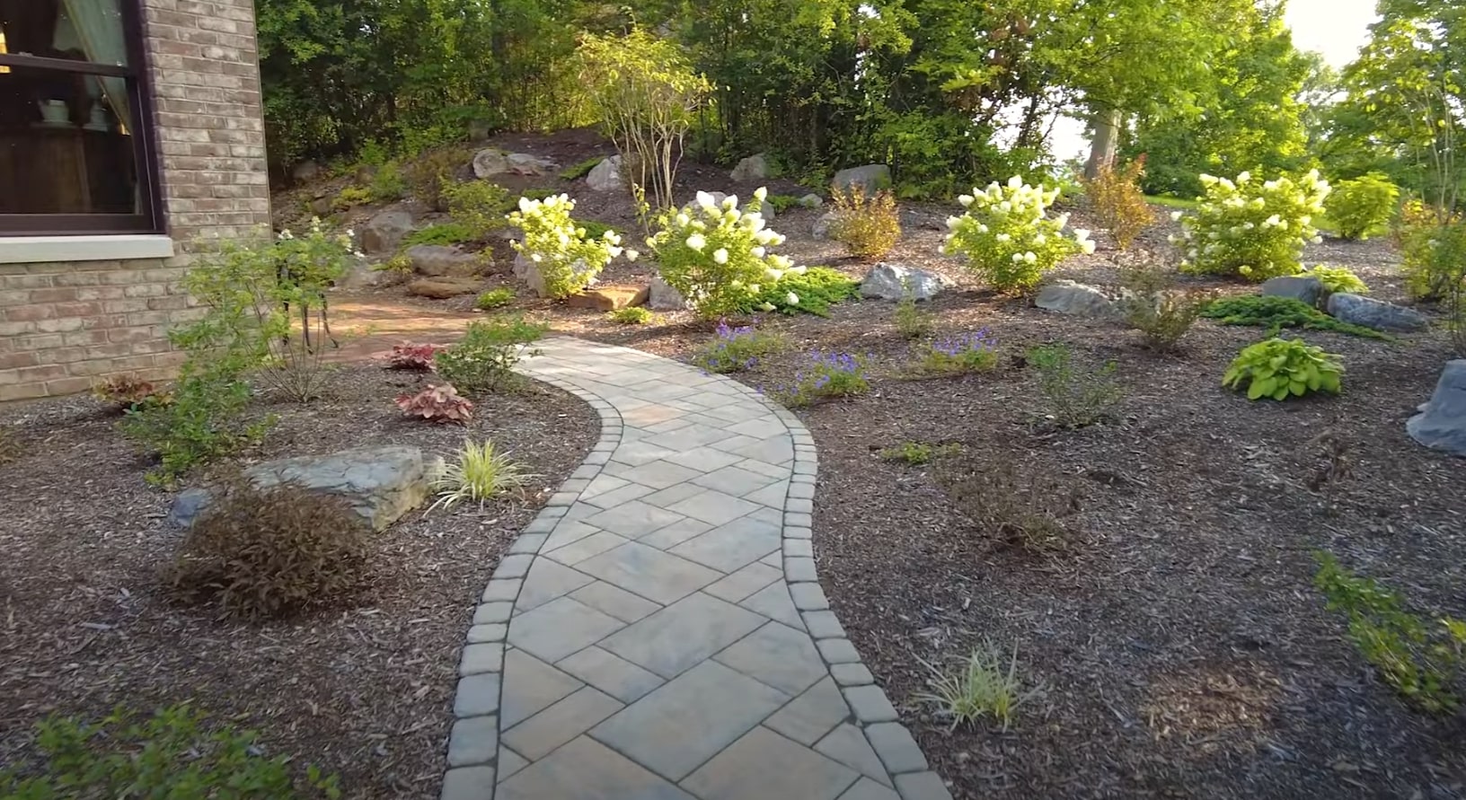 Curved stone paver walkway through professionally landscaped garden beds with ornamental plants and lighting