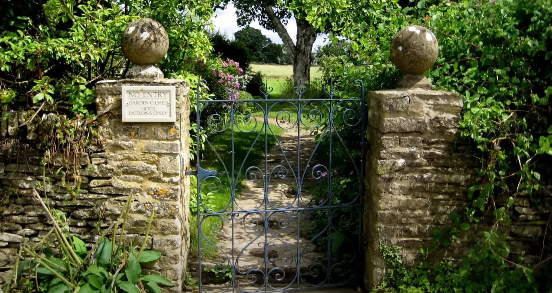 Traditional stone garden entrance with decorative iron gates and mature landscaping design